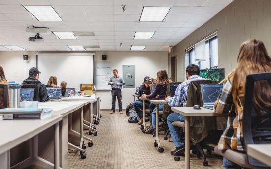 A classroom full of students with the instructor at the front of the room drawing their attention